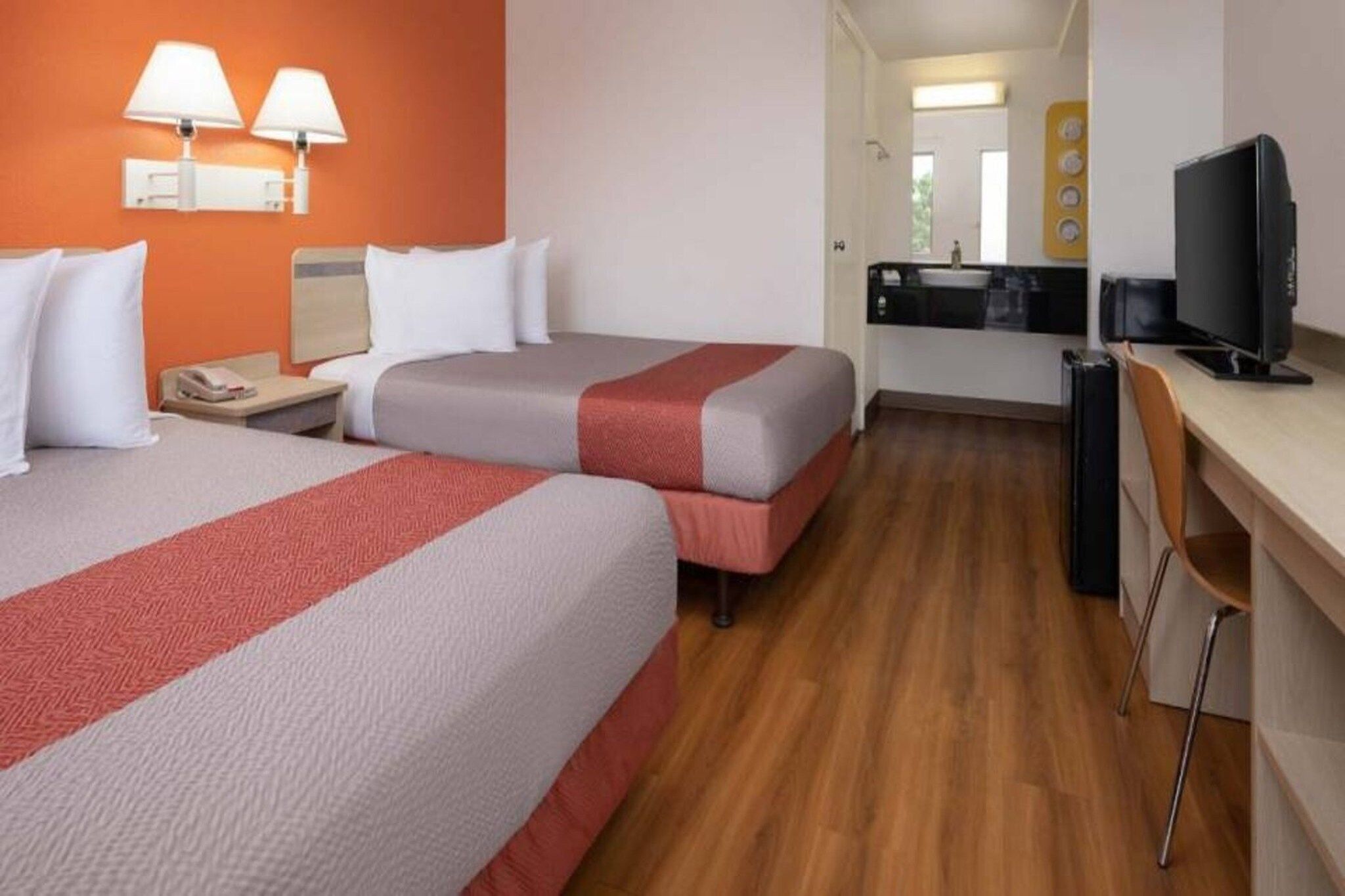 A hotel room with two beds, a desk, a chair, and a television.