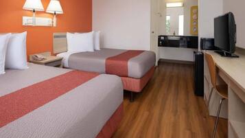A hotel room with two beds, a desk, a chair, and a television.