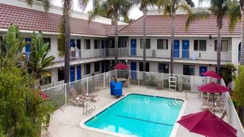 A hotel with a swimming pool, outdoor seating, and palm trees.