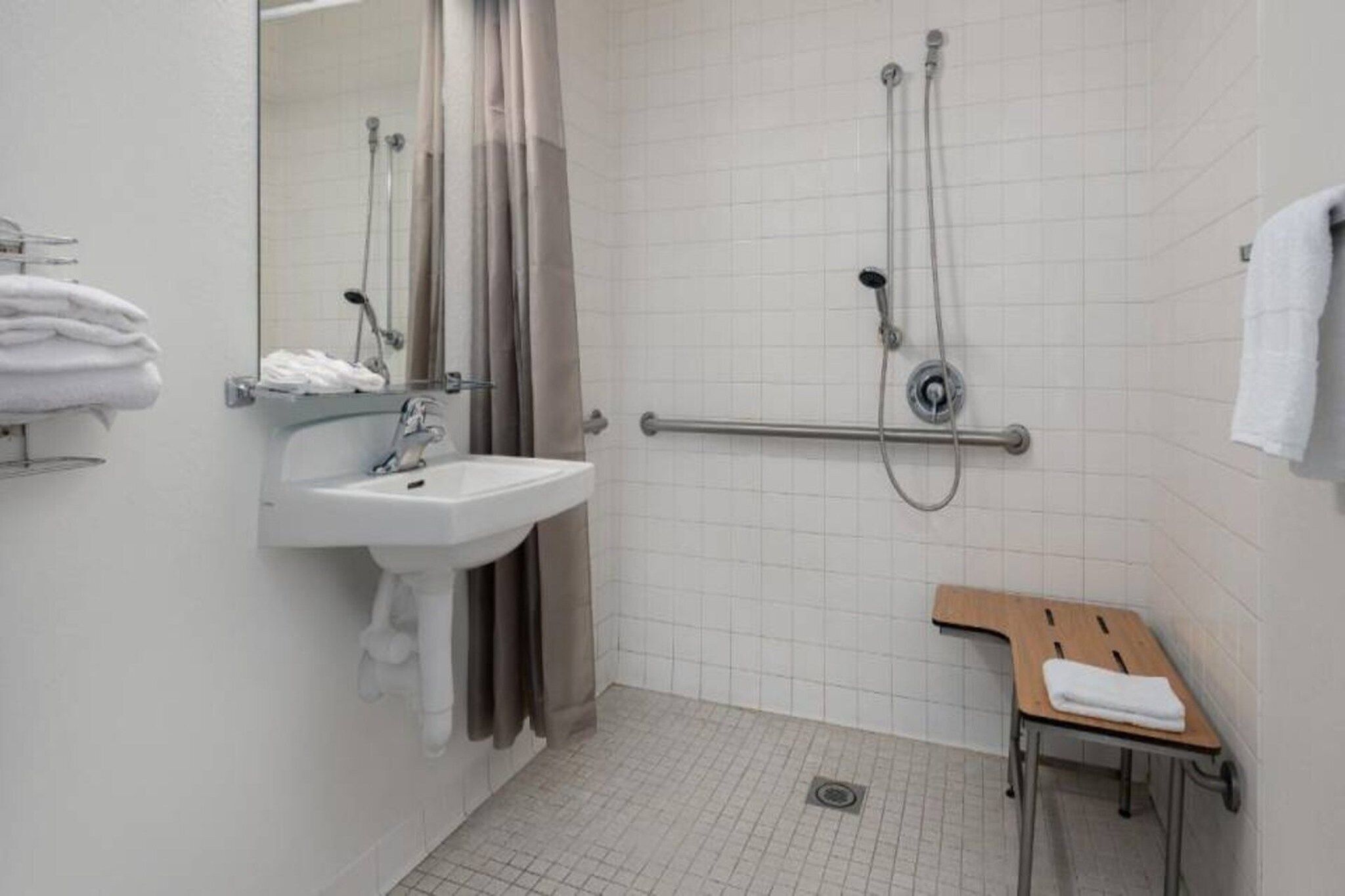 Ein Badezimmer mit Waschbecken, einer Dusche inklusive Haltegriff, einer hölzernen Sitzbank und einem Handtuchhalter.