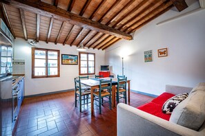 A spacious kitchen with wooden beams, a dining area with a table and chairs, and a red cushioned sofa. - Santa Maria (Florence)