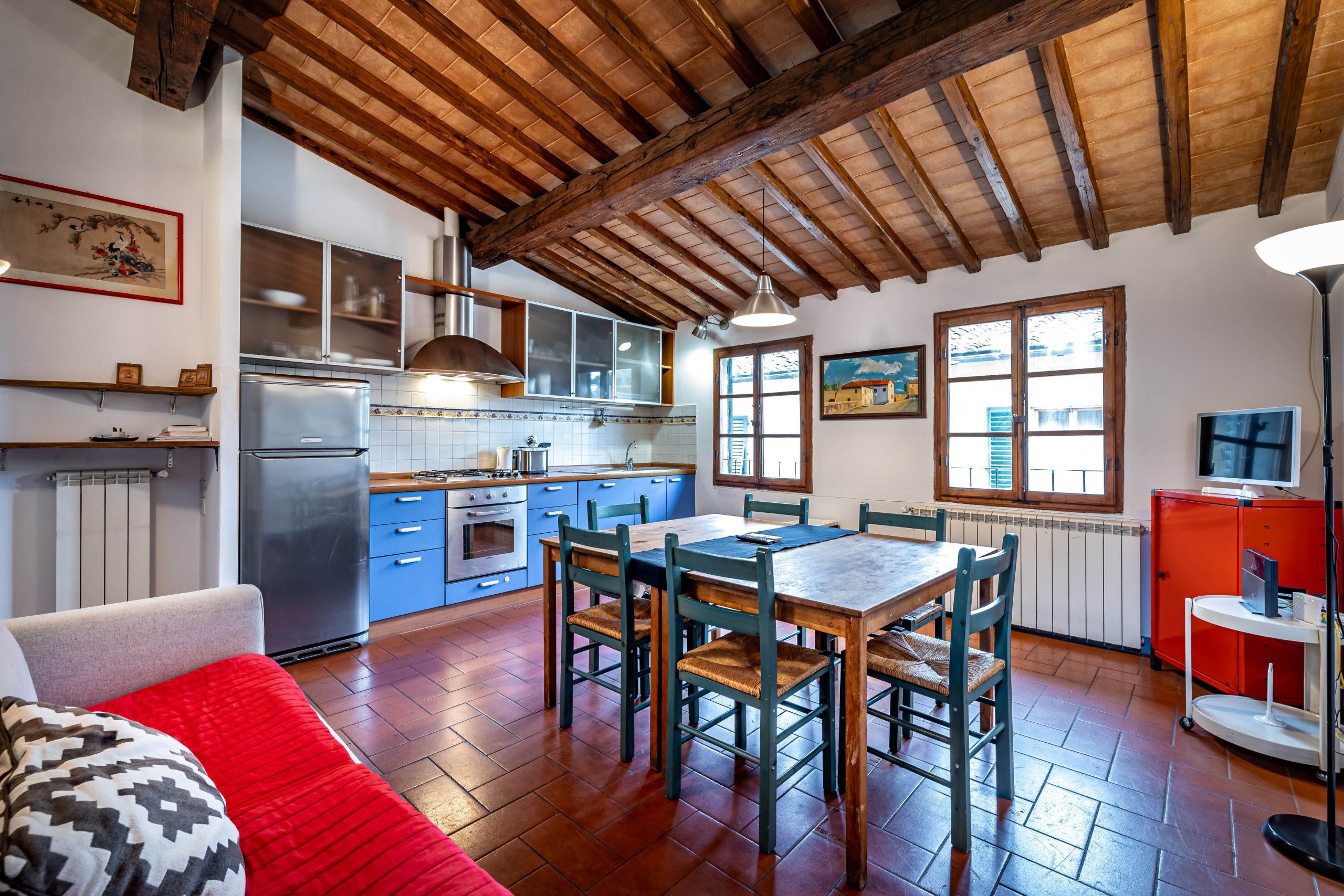Una cocina amplia con vigas de madera, un comedor con sillas y un sofá rojo.