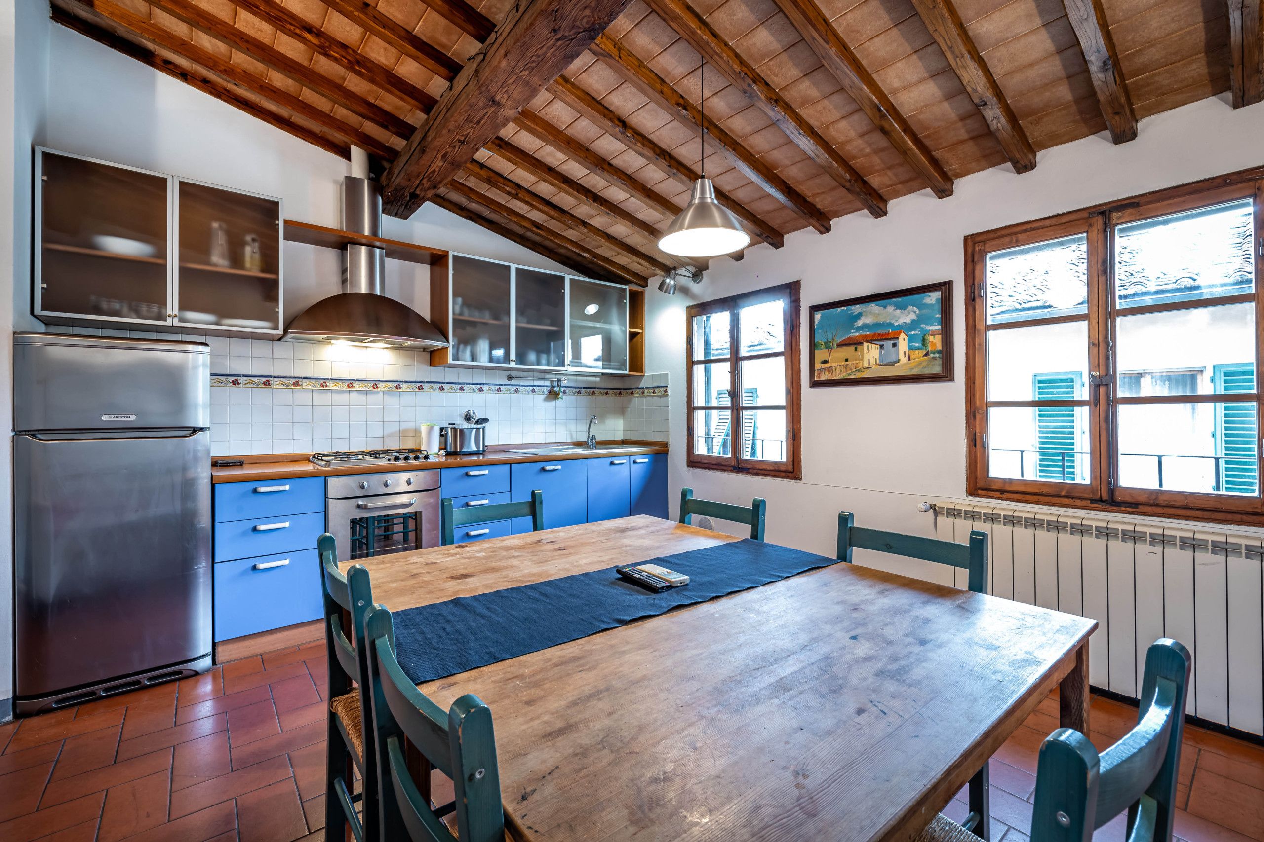 Una cocina con vigas de madera, un refrigerador de acero inoxidable, armarios azules y una mesa de comedor de madera.