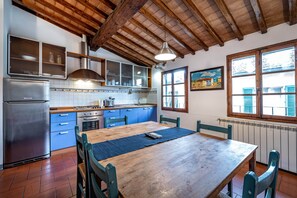 Una cocina con vigas de madera, un refrigerador de acero inoxidable, armarios azules y una mesa de comedor de madera.