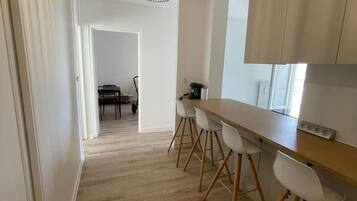 A modern kitchen with a wooden countertop, white chairs, and a pendant light.