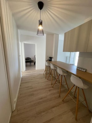 A modern kitchen with a wooden countertop, white chairs, and a pendant light. - The Reims Getaway: City Center - Tram - Balcony & Wi-Fi (Reims)