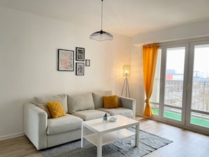 A modern living room with a sofa, a coffee table, and a floor lamp. - The Reims Getaway: City Center - Tram - Balcony & Wi-Fi (Reims)