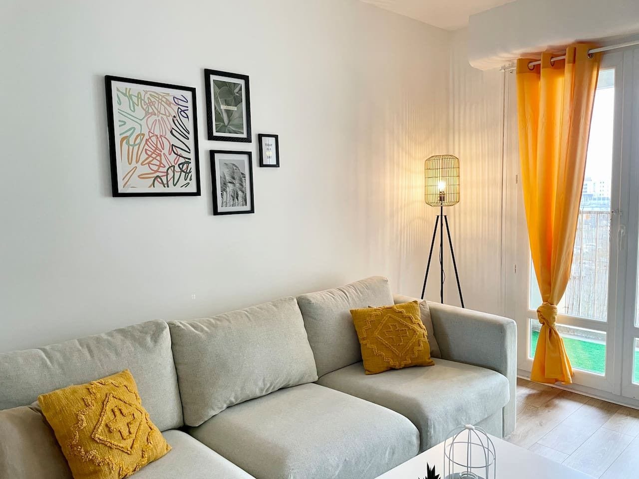 A living room with a sofa, two cushions, a floor lamp, and framed artwork on the wall.
