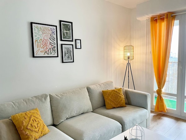 A living room with a sofa, two cushions, a floor lamp, and framed artwork on the wall. - The Reims Getaway: City Center - Tram - Balcony & Wi-Fi (Reims)