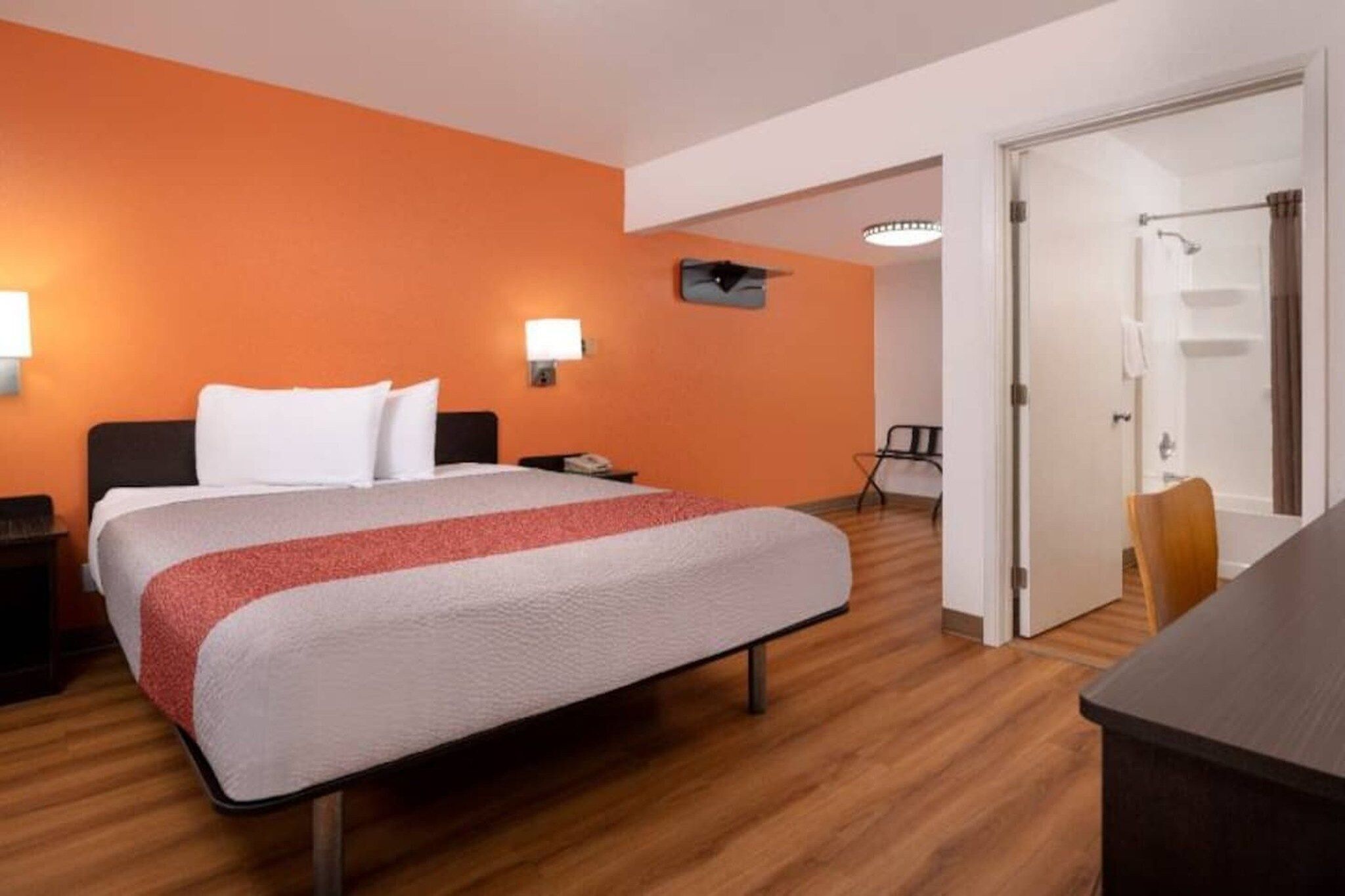 Quarto de hotel com cama, mesa de cabeceira, escrivaninha, cadeira e porta para um banheiro.