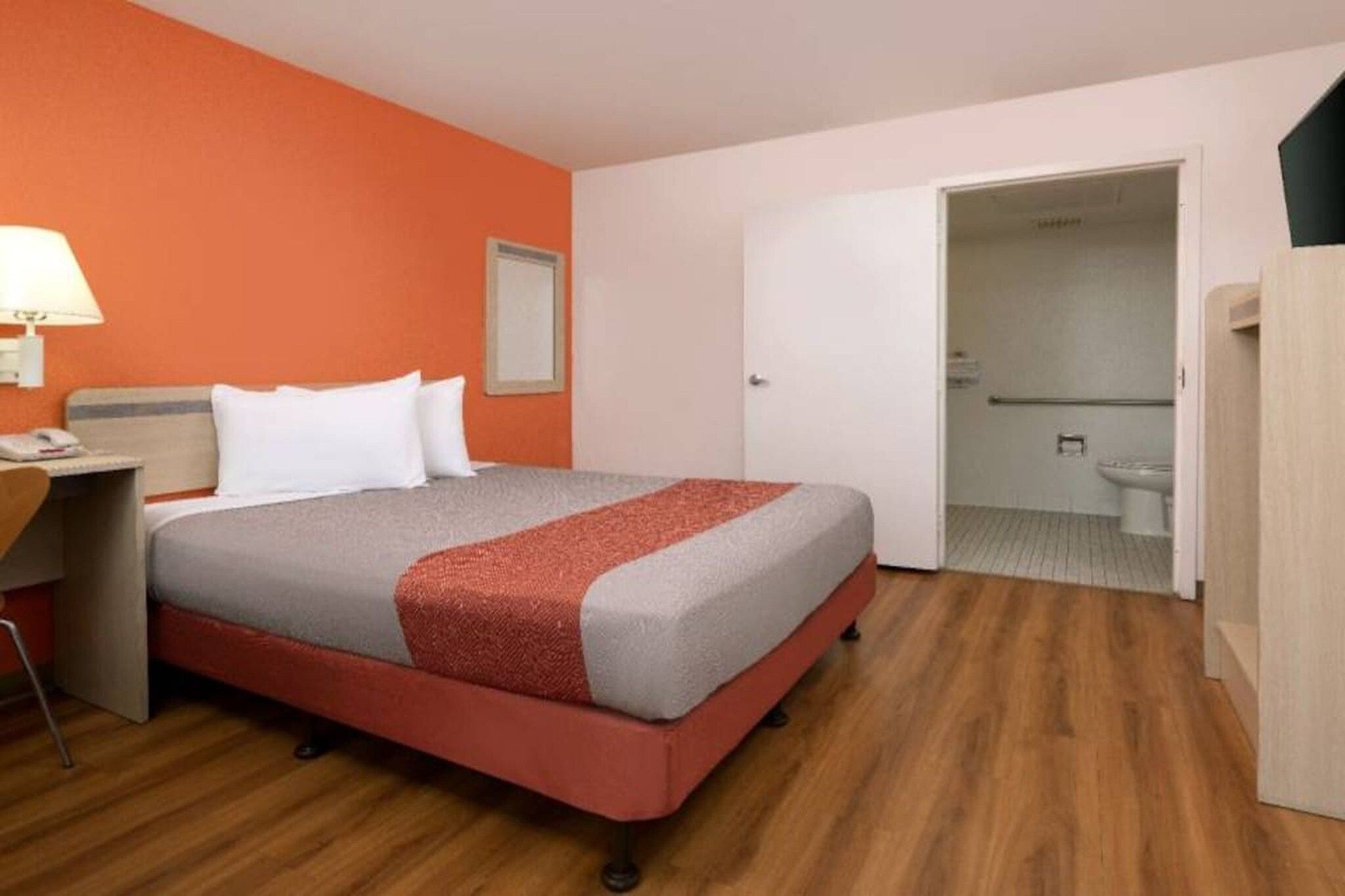 A hotel room with a bed, a desk, and a bathroom visible through an open door.
