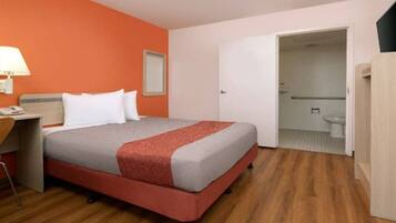 A hotel room with a bed, a desk, and a bathroom visible through an open door.