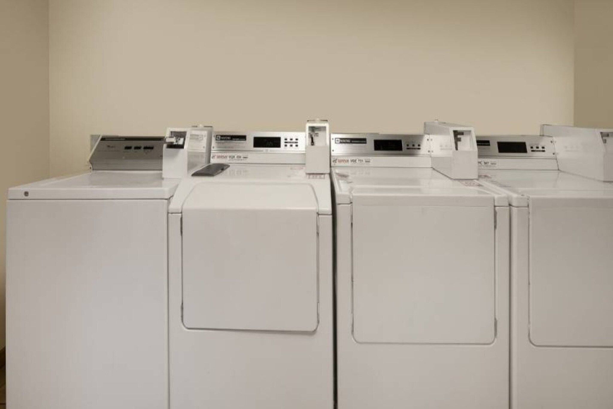 A row of white, front-loading washing machines in a room with plain walls.