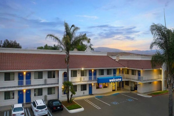 Un motel con un letrero que dice 'welcome', varios pisos y un estacionamiento.