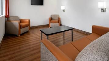 A modern hotel room with a wooden floor, two sofas, a coffee table, and a flat-screen TV mounted on the wall.