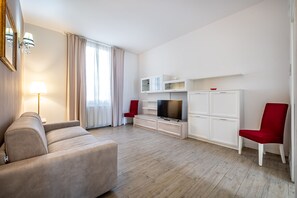 Una sala moderna con sofá, televisión, armarios y una butaca roja.