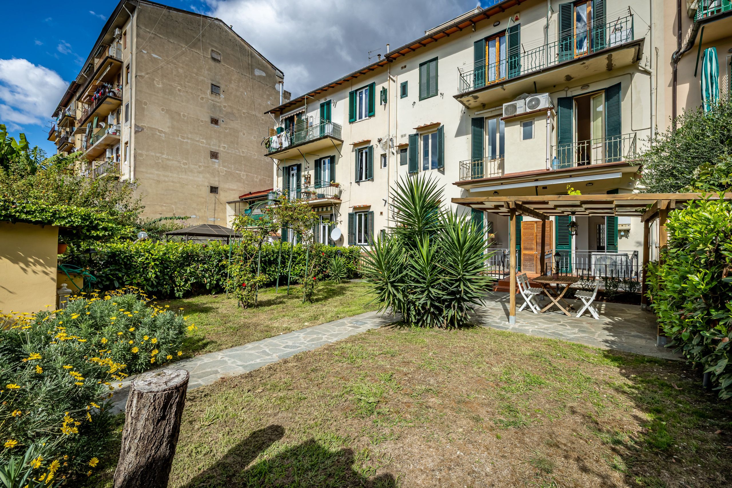 Ein Innenhof mit Garten, Sitzgelegenheiten im Freien und einem Gebäude mit mehreren Balkonen.