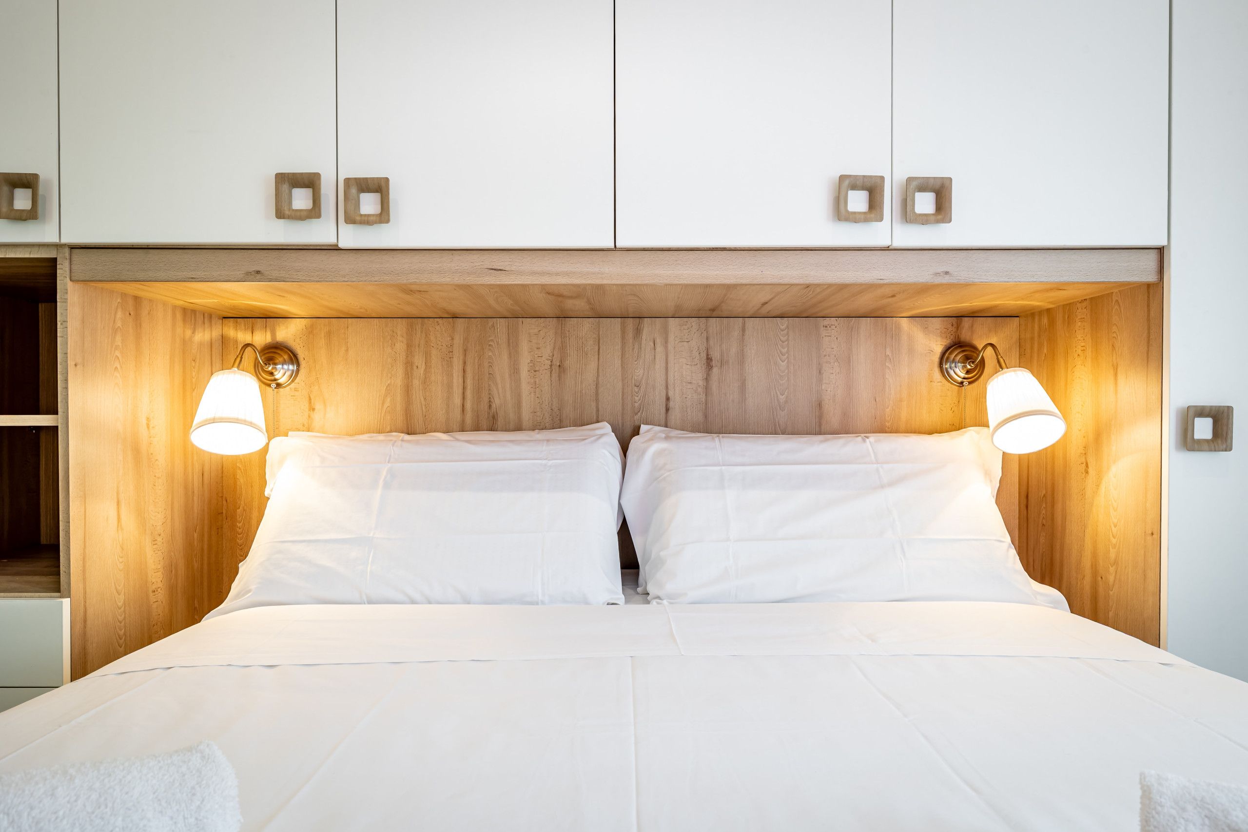 A bed with two pillows, a wooden headboard, and two wall-mounted lamps.
