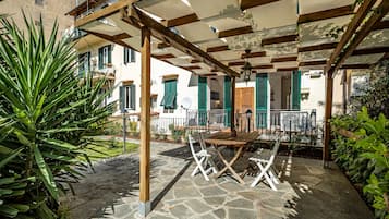 Area patio esterna con pergola in legno, pavimento in pietra e mobili bianchi.