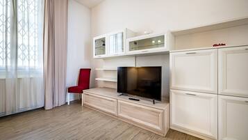 A modern living room with a flat-screen TV on a wooden cabinet, a red chair, and a large window with sheer curtains.