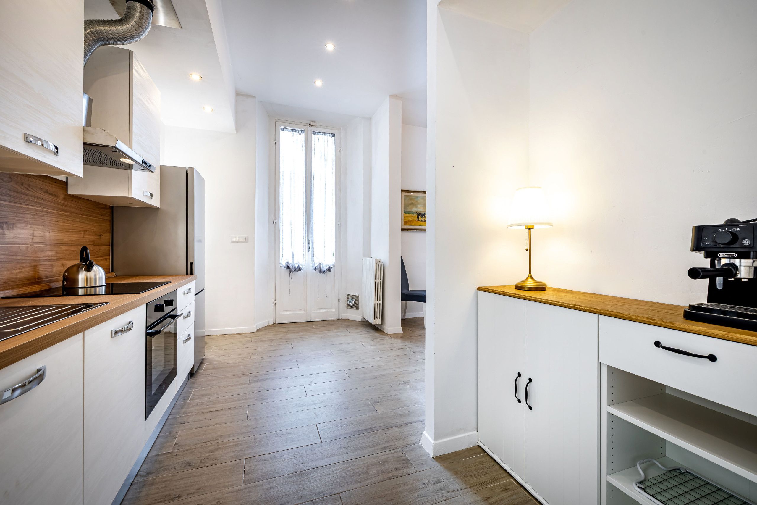 A modern kitchen with white cabinetry, a wooden countertop, and a coffee machine.
