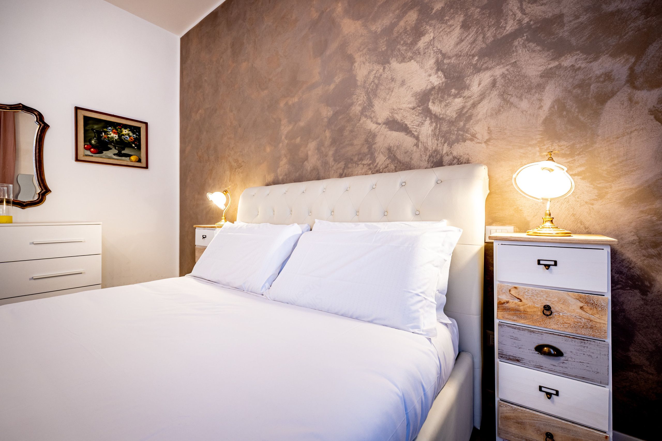 A bedroom with a bed, two bedside tables, a dresser, a mirror, and a framed picture on the wall.