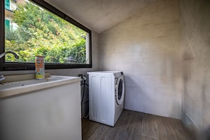 Uma área de lavanderia compacta, com máquina de lavar, secadora e janela com vista para o verde.
