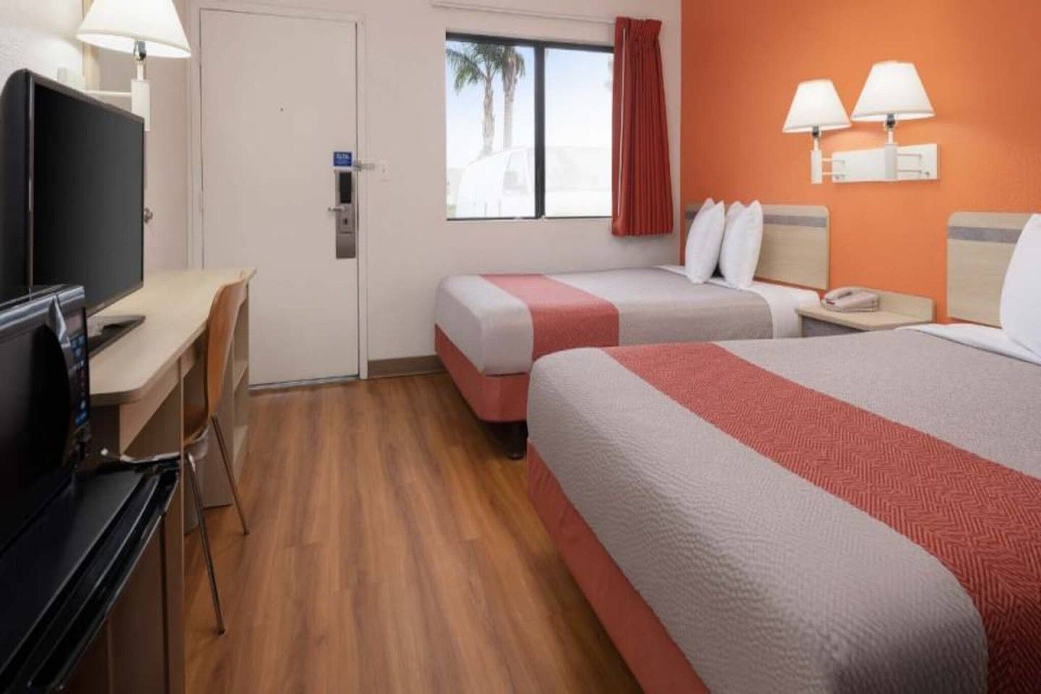 A hotel room with a desk, two beds, a television, and a window with curtains.