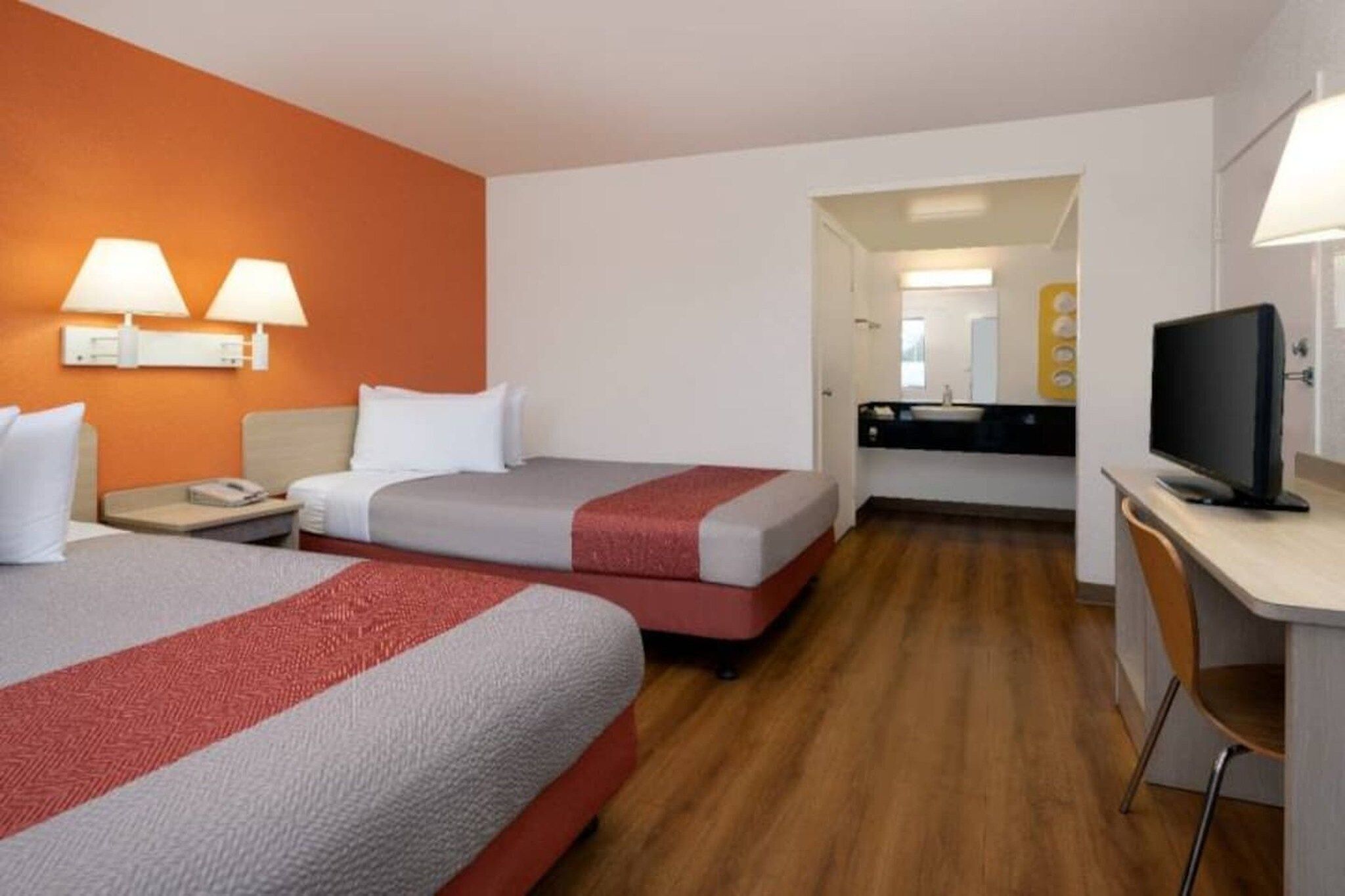 A hotel room with two beds, a desk, a television, and a bathroom visible through an open door.
