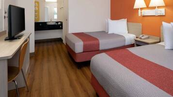 Quarto de hotel com duas camas, uma escrivaninha, televisão e banheiro.
