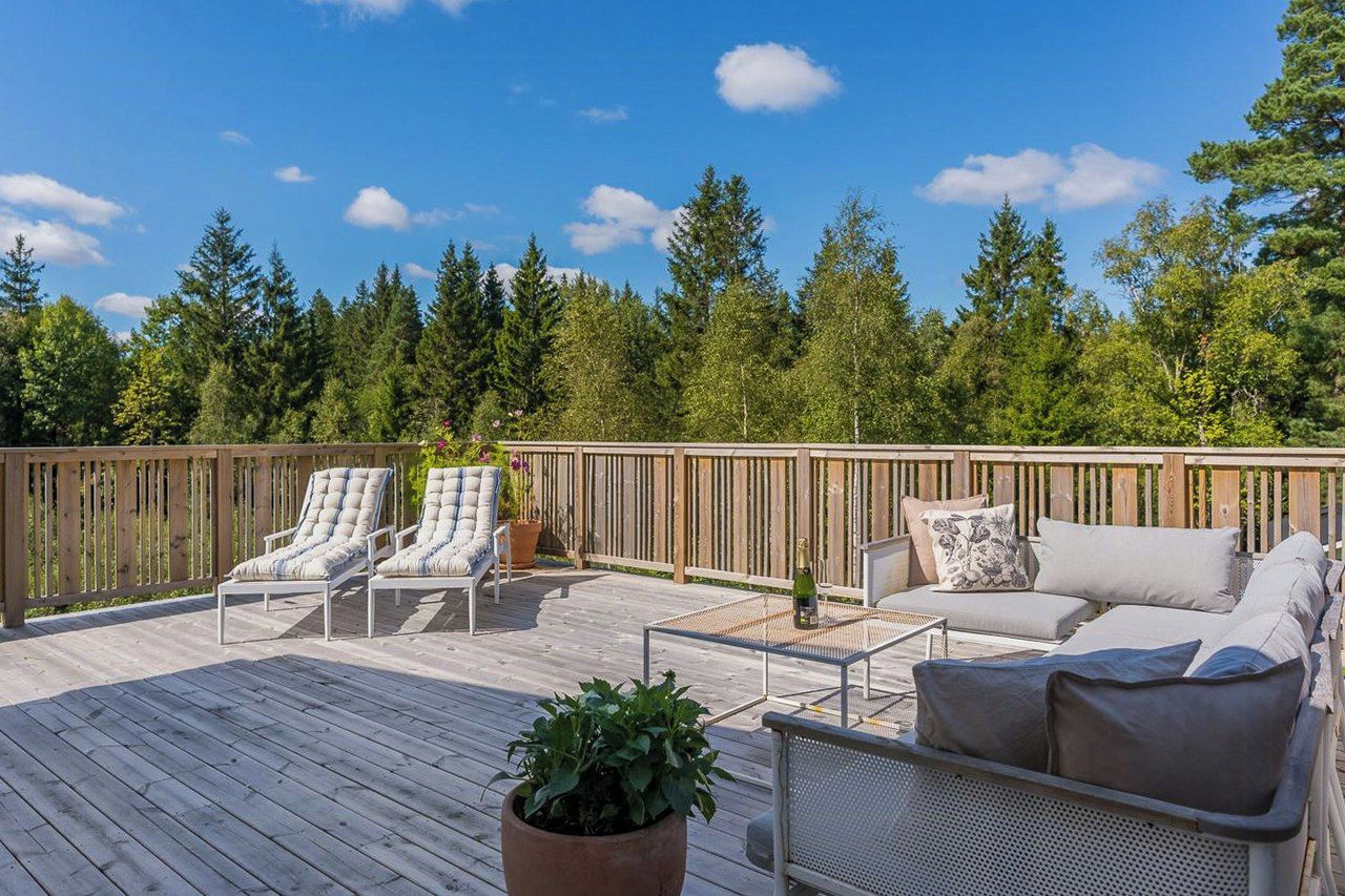 Una terraza de madera con sillones y un sofá, rodeada por una valla de madera y árboles.
