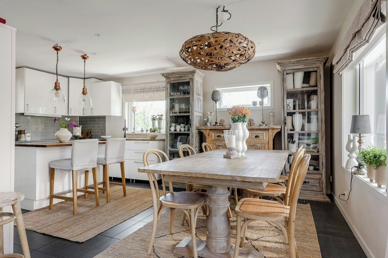 Een moderne keuken met witte kastjes, een houten eettafel en een hangende rieten lamp.