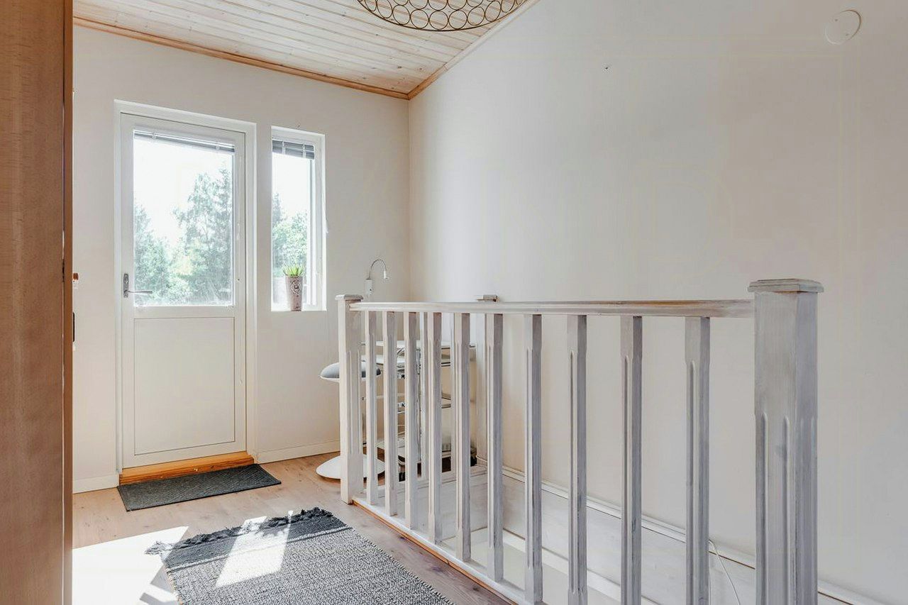 A clean, minimalist hallway with a white door, a small window, and a metal railing.