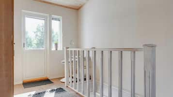 A clean, minimalist hallway with a white door, a small window, and a metal railing.