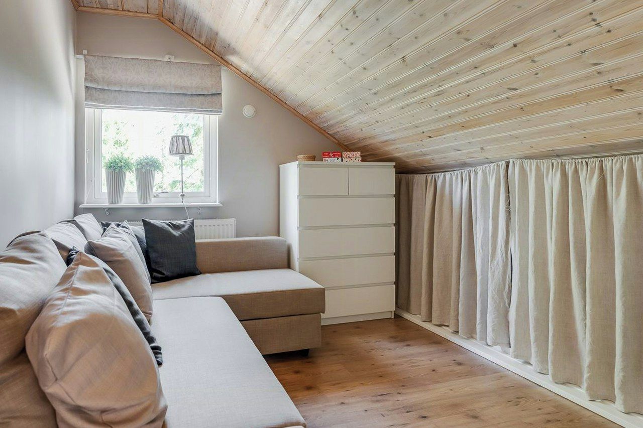 Una stanza con soffitto in legno, un divano, un armadio, una finestra con tende e un termosifone.