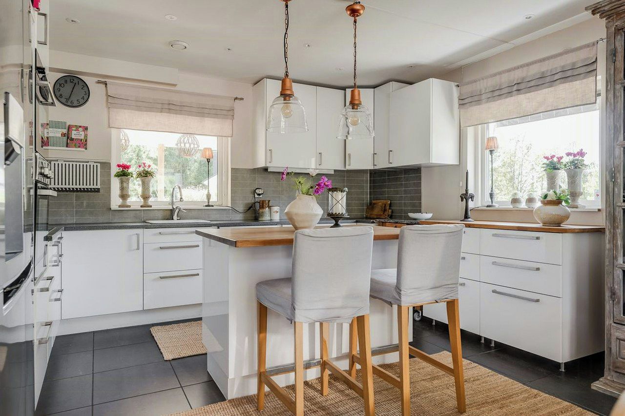 A modern kitchen with white cabinetry, a central island with bar stools, pendant lighting, and a view through the window.