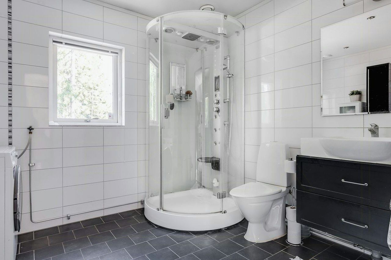 Een moderne badkamer met een douchecabine van glas, een wit toilet en een zwarte wastafel met lades.