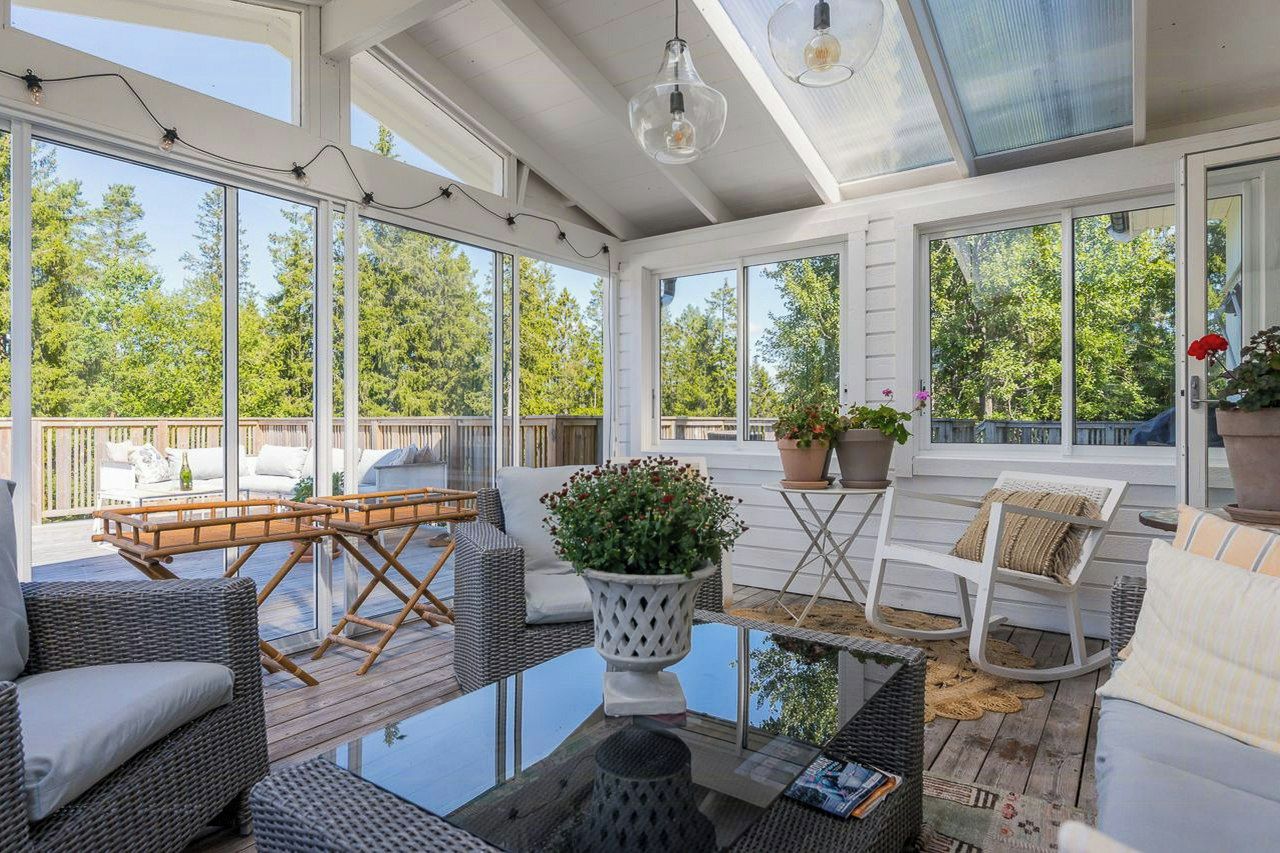 A sunlit room with a glass ceiling, wicker furniture, and potted plants.