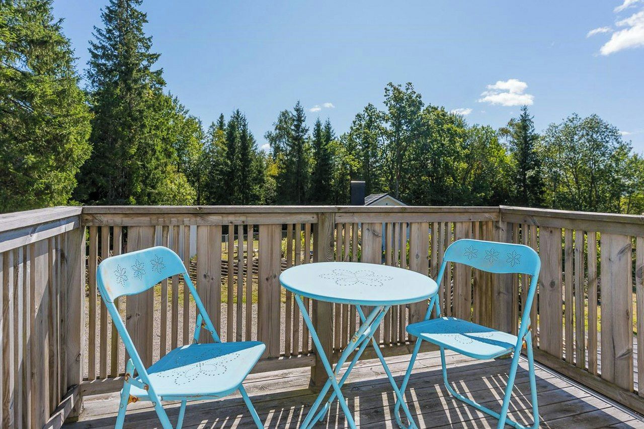 A wooden deck with two chairs and a small table, surrounded by a wooden fence and trees.