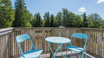 A wooden deck with two chairs and a small table, surrounded by a wooden fence and trees.