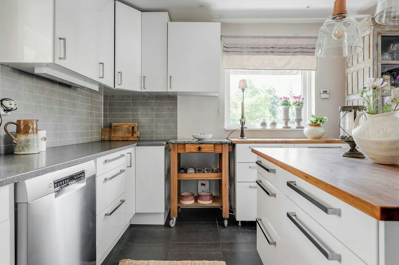 Una cocina moderna con armarios blancos, encimera de madera y ventana con vistas a zonas verdes.