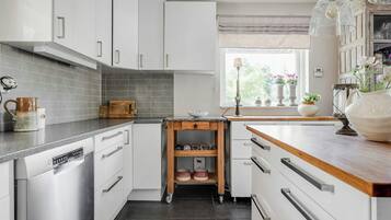 Una cocina moderna con armarios blancos, encimera de madera y ventana con vistas a zonas verdes.