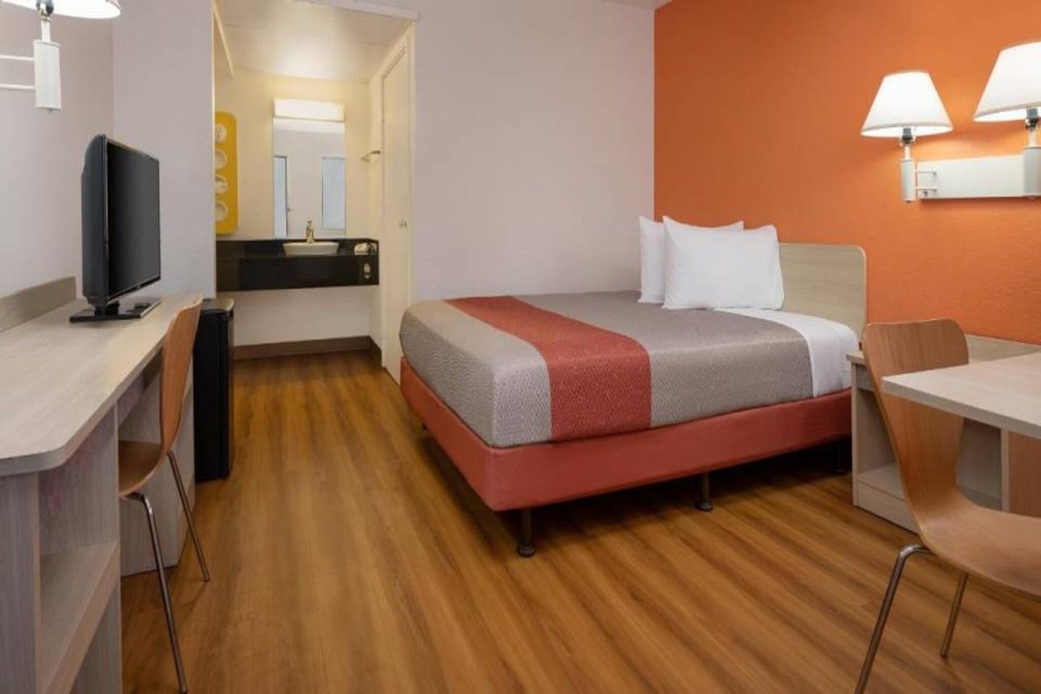 A hotel room with a bed, desk, chair, and a television.