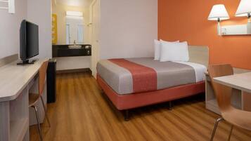 A hotel room with a bed, desk, chair, and a television.