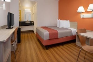 Quarto de hotel com cama, escrivaninha, cadeira e televisão.