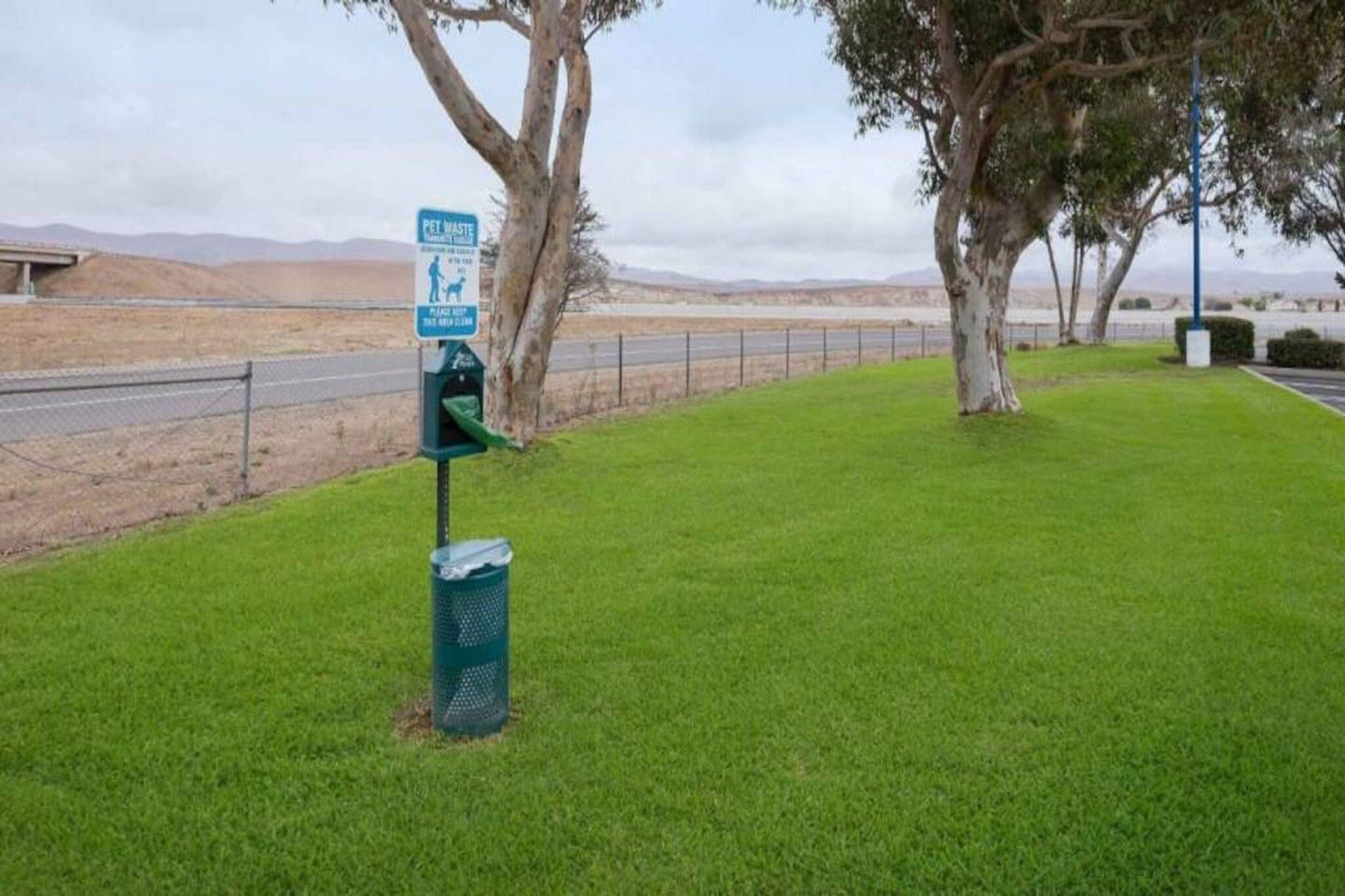 Área gramada com estação de recolha de resíduos de animais de estimação e sinalização de sua utilização.