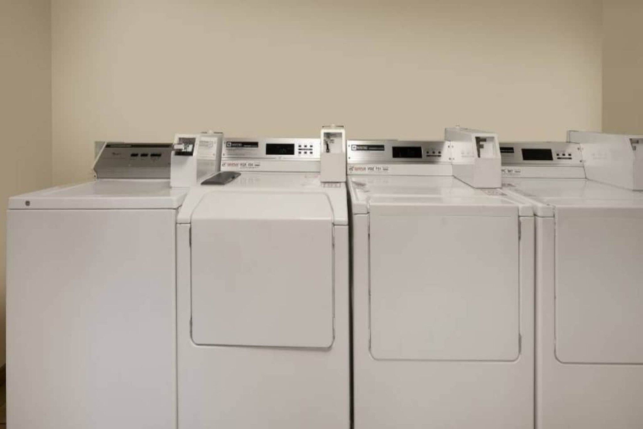 A row of white, front-loading washing machines in a room with plain walls.