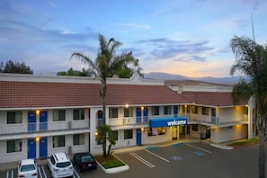 Um motel com um letreiro de 'bem-vindo', vários andares e um estacionamento.