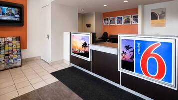 A hotel reception area with a digital screen displaying a news channel, a reception desk, and a wall with framed pictures.