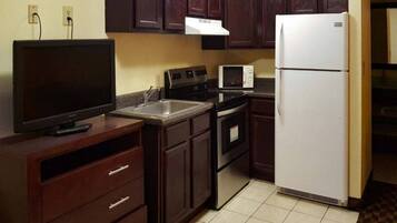 Una cocina con armarios de madera oscura, un refrigerador blanco, un microondas, un horno y un televisor sobre un mueble de madera.